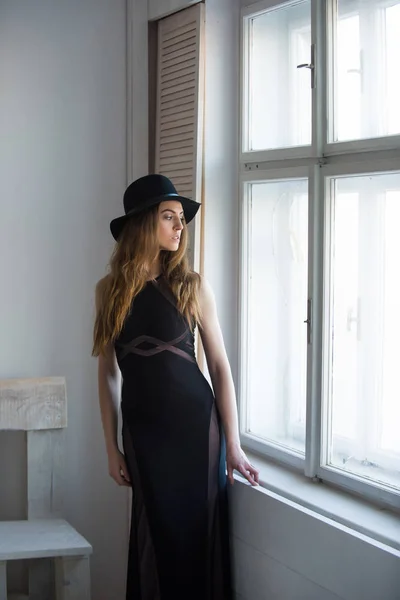 Pretty girl in hat and dress at chair and window — Stock Photo, Image