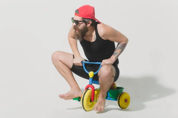 Bearded shouting man on colorful bicycle toy in sunglasses, cap — Stock Photo, Image