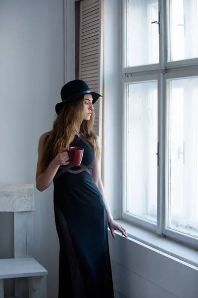 Menina bonita em chapéu e vestido na cadeira e janela — Fotografia de Stock