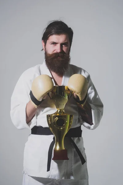 Bearded smiling karate man in kimono, boxing gloves, champion cup — Stock Photo, Image