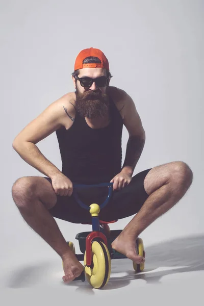Bearded happy man on colorful bicycle toy in sunglasses, cap — Stock Photo, Image