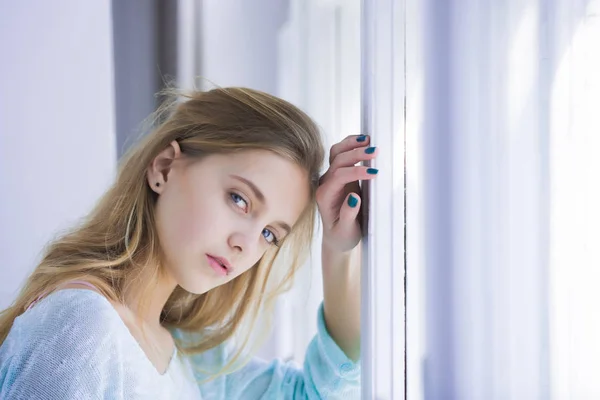 Chica bonita con ojos azules de pie en la ventana — Foto de Stock