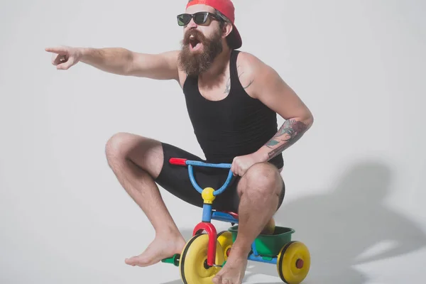Barbudo gritando homem no colorido bicicleta brinquedo em óculos de sol, cap — Fotografia de Stock