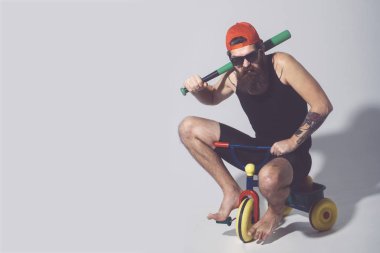 Sakallı kızgın adam yeşil beysbol sopası Bisiklet oyuncak üzerinde tutar.