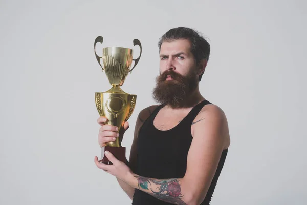 Bärtiger ernster Mann hält goldenen Meisterpokal auf grauem Hintergrund — Stockfoto