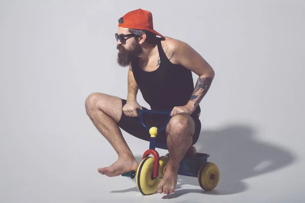 Bearded man on colorful bicycle toy in red cap sungsses — Stock Photo, Image