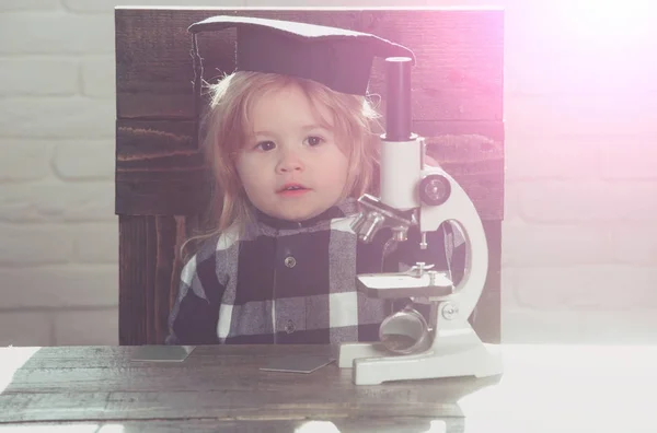 Menino pequeno, criança cientista em chapéu de graduação com microscópio — Fotografia de Stock