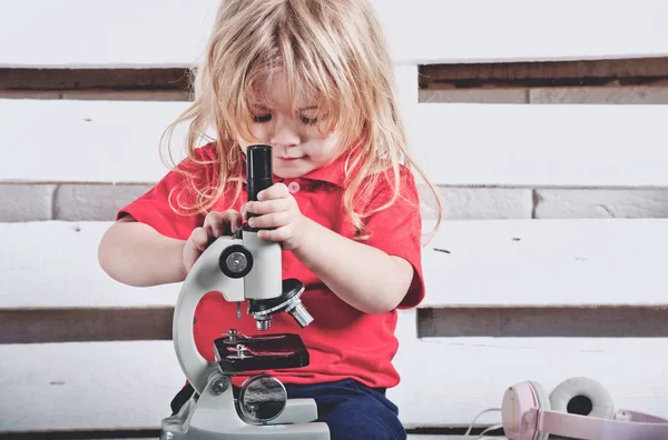 Menino pequeno com microscópio e fone de ouvido em fundo de madeira — Fotografia de Stock