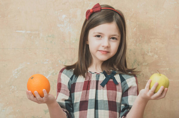 child or girl holding orange and apple in hands