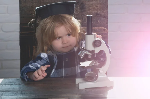 Niño pequeño, científico niño en sombrero de graduación con microscopio —  Fotos de Stock