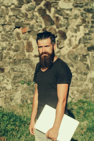 Hombre barbudo con barba larga de pie con portátil gris — Foto de Stock