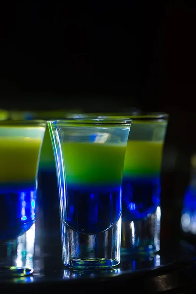 Cócteles o tiradores en capas azules y amarillas en vasos de chupito — Foto de Stock