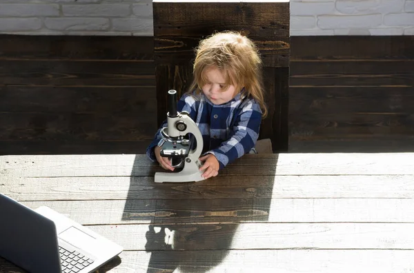 Concepto educativo, niño estudiante que estudia en el lugar de trabajo con microscopio, computadora portátil — Foto de Stock