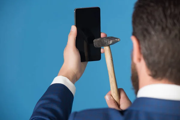 Mies halkeamia älypuhelin vasaralla, rikki puhelin sinisellä taustalla — kuvapankkivalokuva