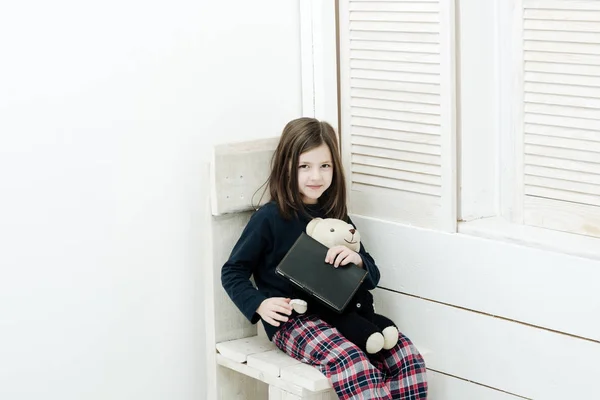 Niña cariñosa sentada con cuaderno y osito de peluche — Foto de Stock