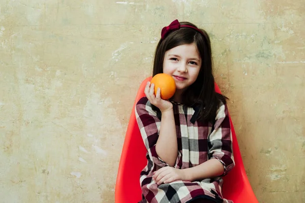 Chica alegre con naranja en la mano sonriendo en silla de plástico — Foto de Stock