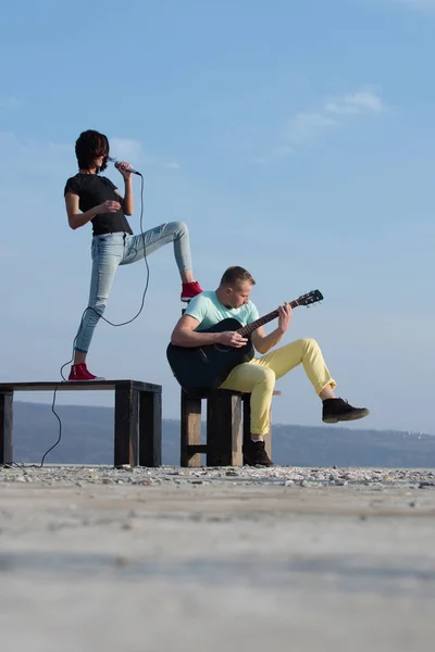 Linda chica cantando con un hombre guapo apuntando al cielo azul — Foto de Stock