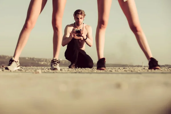 Мускулистый мужчина, фотограф с фотоаппаратом и сексуальными ногами женщин — стоковое фото