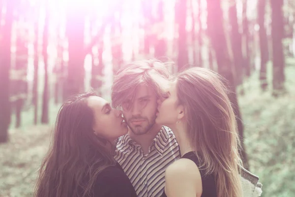 Zwei hübsche Frauen küssen bärtigen Mann im Wald — Stockfoto