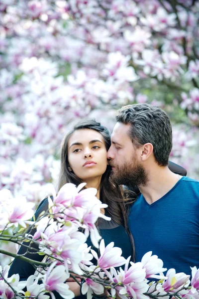 Homem beijando menina bonita em árvores florescentes com magnólia — Fotografia de Stock