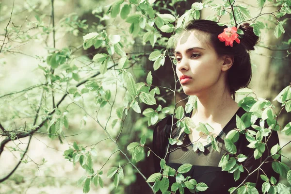 Menina com flor no cabelo em folhas de árvore verde — Fotografia de Stock