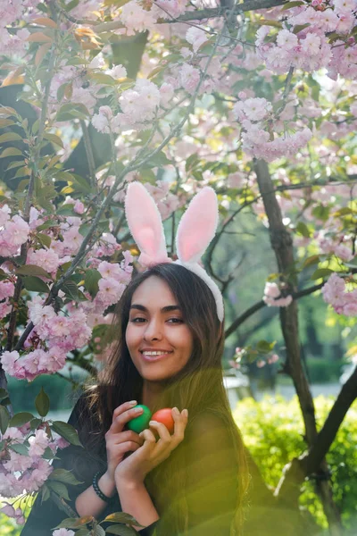 Vrouw met bunny oren glimlachend met gekleurde eieren, sakura — Stockfoto