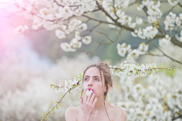 Beautiful young woman enjoying smell in a flowering spring garden