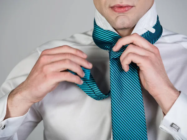 Чоловік зав'язує смугасту краватку в білій сорочці — стокове фото