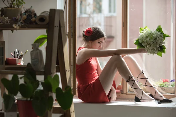 Молода дівчина в червоній сукні в оранжереї з квіткою — стокове фото