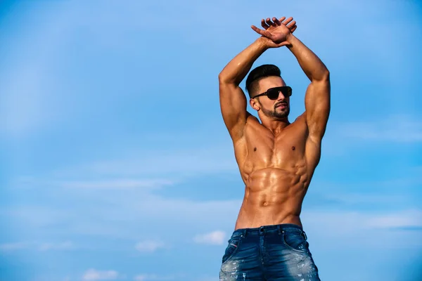 Guy with muscular body in sunglasses on blue sky — Stock Photo, Image