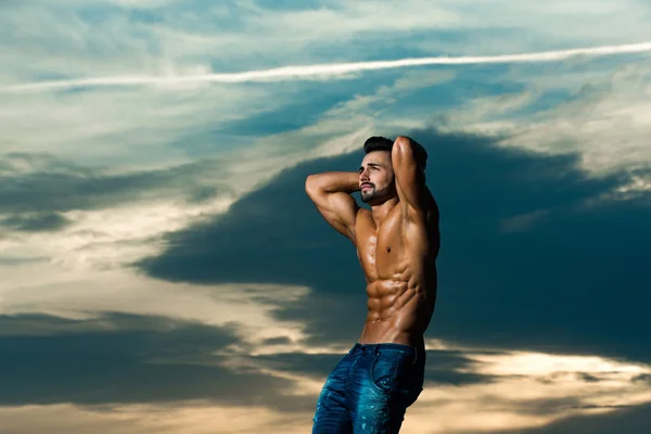 Muscular man with muscle torso on cloudy sunset sky background — Stock Photo, Image