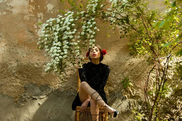 Mujer sentada en silla de mimbre bajo flores florecientes — Foto de Stock