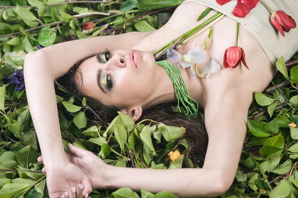 Frau mit modischem Make-up mit Blüten auf grünen Blättern — Stockfoto