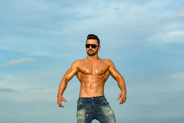 Sexy man with muscular body in sunglasses on blue sky — Stock Photo, Image