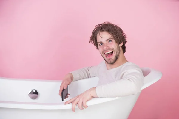 Uomo sorridente nella vasca da bagno con cellulare — Foto Stock