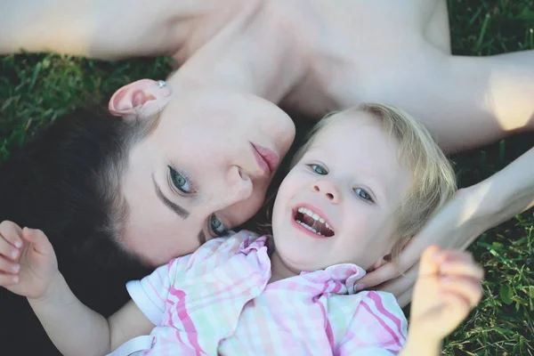 Sorridente ragazzo carino e bella madre sdraiata su erba verde — Foto Stock