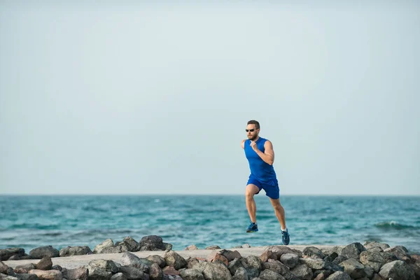 Homme coureur avec beau visage courant le long de la côte de pierre — Photo