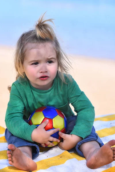 Chłopiec siedzi i gra z piłką na plaży — Zdjęcie stockowe