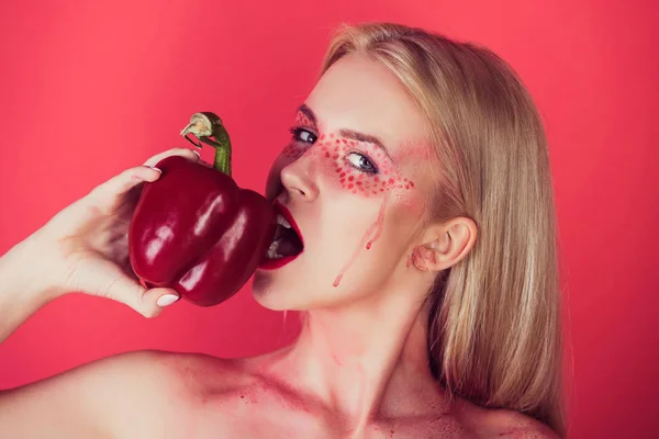 Blonde žena s kreativní módní make-up kousnutí paprika — Stock fotografie