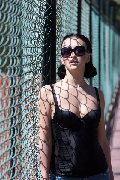 Kvinne sexy brunette i svarte solbriller og badedrakt nær gjerde – stockfoto