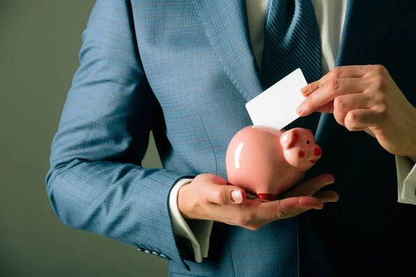 Mãos masculinas colocando cartão de visita no banco porquinho para salvar — Fotografia de Stock