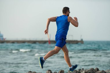 Güzel plaj boyunca çalışan yakışıklı runner genç adam atlet