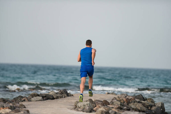 Бегун в синей спортивной одежде бежит вдоль побережья
