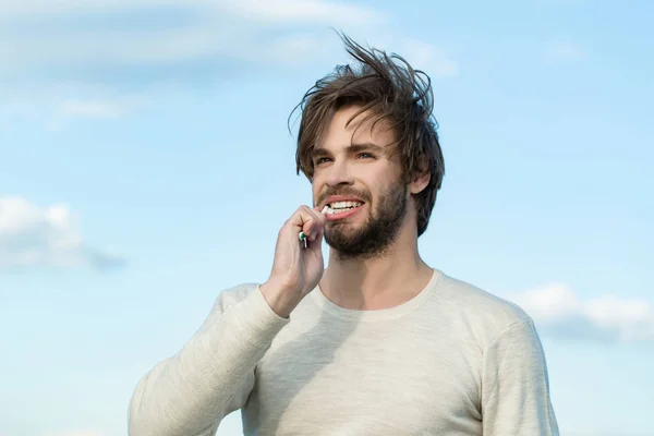 Hombre feliz cepillar los dientes con pasta de dientes en el cielo azul, metrosexual —  Fotos de Stock