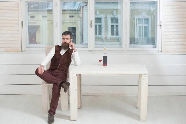 Hipster siedzi na krześle przy stole z butelki i kieliszki — Zdjęcie stockowe