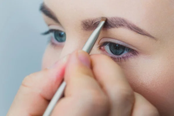 Mulher com olhos azuis recebendo maquiagem nas sobrancelhas — Fotografia de Stock