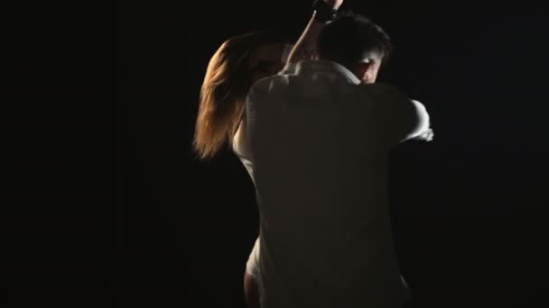 Δυο χοροί σε μαύρο φόντο, τύπος τραγουδά νεαρή κοπέλα σε λευκό μαγιό, άνθρωπος σε λευκό πουκάμισο, τραγούδι, μουσική βίντεο για ρομαντική μουσική τραγουδιστής. Σέξι ζευγάρι στο στούντιο το βράδυ κάνει παθιασμένο χορό — Αρχείο Βίντεο