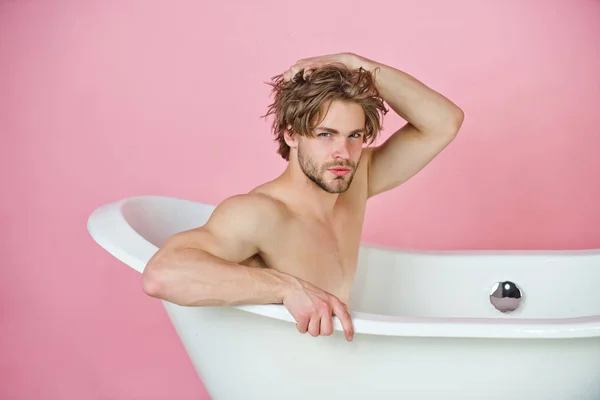 Cara com corpo muscular sentado na banheira branca — Fotografia de Stock