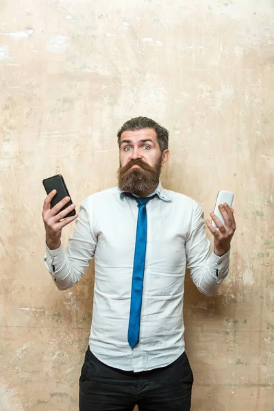 Hipster tai parrakas mies vertailla matkapuhelin ja älypuhelin — kuvapankkivalokuva