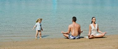 Anne, baba ve çocuk kumsalda yoga egzersizleri yapıyor